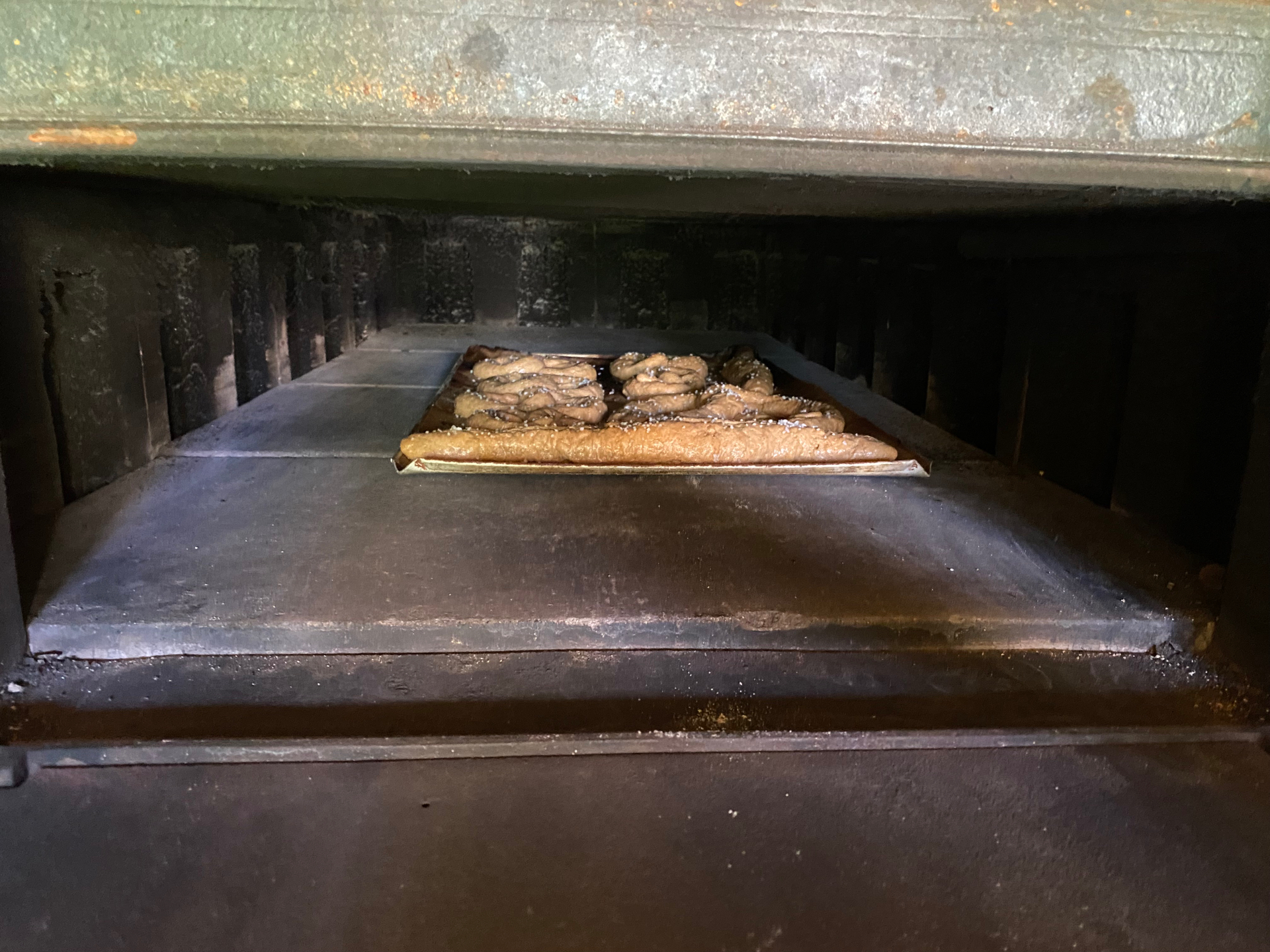 Blech mit Brezen im dunklen Holzbackofen kurz vor dem Backen